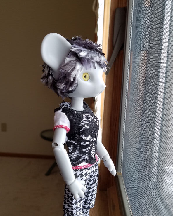 A grey Hujoo Phoebe Mouse doll standing looking out the window. She has a short hairstyle of choppy layers of patchy silver, steel grey, and black hair. we can see how the hair at the back of her head almost meets the hair in front of her ears.